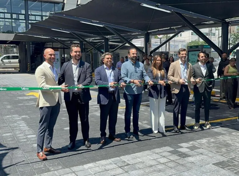 Eight professionally dressed people hold a green ribbon for a ribbon-cutting ceremony outside a glass-front building.
