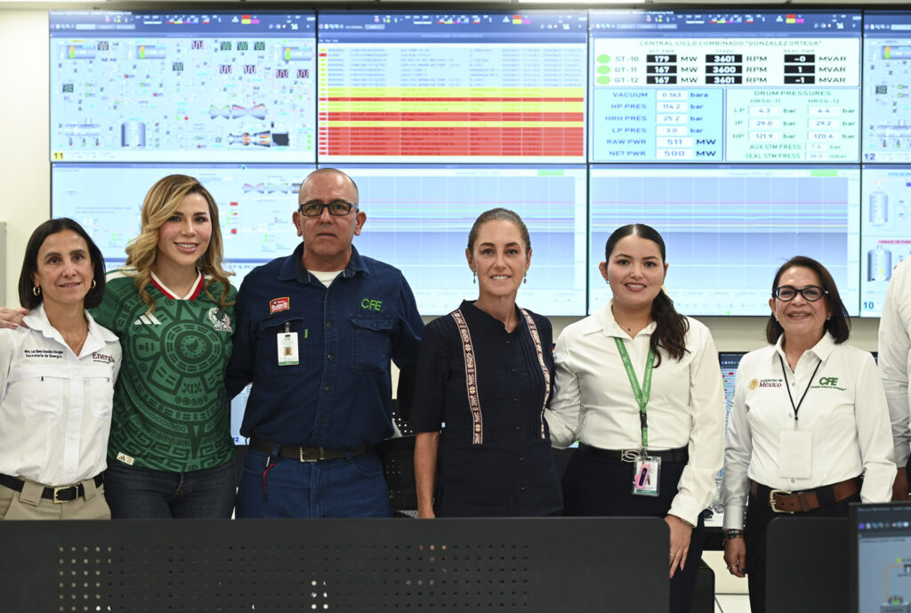 2026-06-21_Inauguraci_n_Central_de_Ciclo_Combinado_Mexicali_30_SLE - Petróleo y Energía Six professionals stand together in a control room with multiple monitor walls displaying graphs and data screens behind them, suggesting a team briefing or operations center setting.