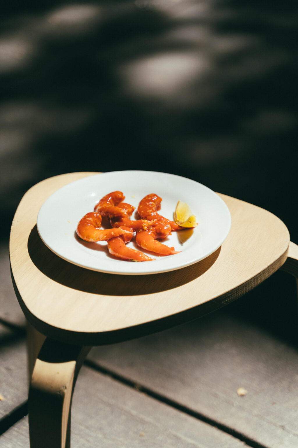 Camarones - Petróleo y Energía Plate with peeled orange shrimp and a lemon wedge on a white dish atop a light wooden table, with a dark blurred background.