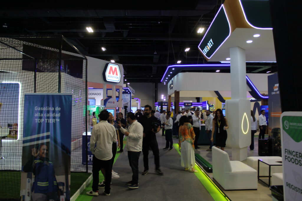 IMG_3127 1 - Petróleo y Energía Busy indoor trade show floor with attendees walking between illuminated booths; visible Marathon sign in the backgroundCN: M Marathon board.