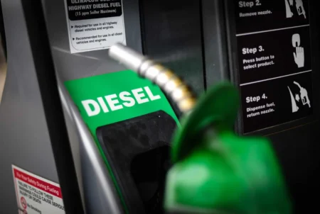 Diesel fuel nozzle inserting into a pump with a bright green 'DIESEL' label visible at the nozzle area.