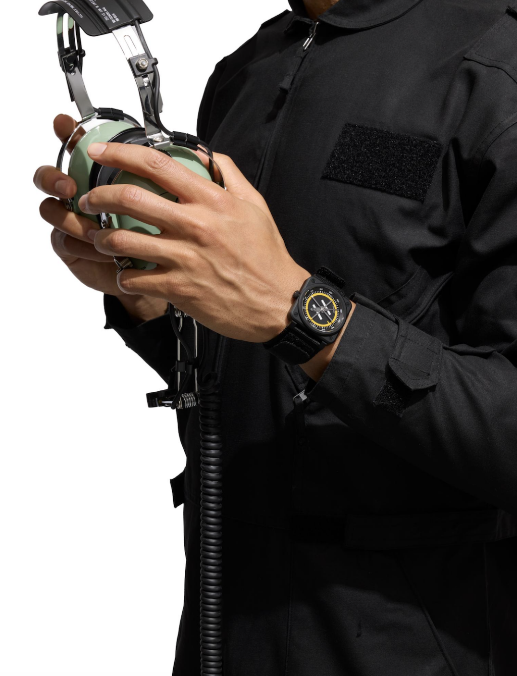 helipad 3 - Petróleo y Energía Person in a black tactical jacket holding an over-ear aviation headset with a coiled cord; wristwatch visible on the left wrist